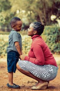 tilt shift lens photography of woman wearing red sweater and white skirt while holding a boy wearing white and black crew neck shirt and blue denim short